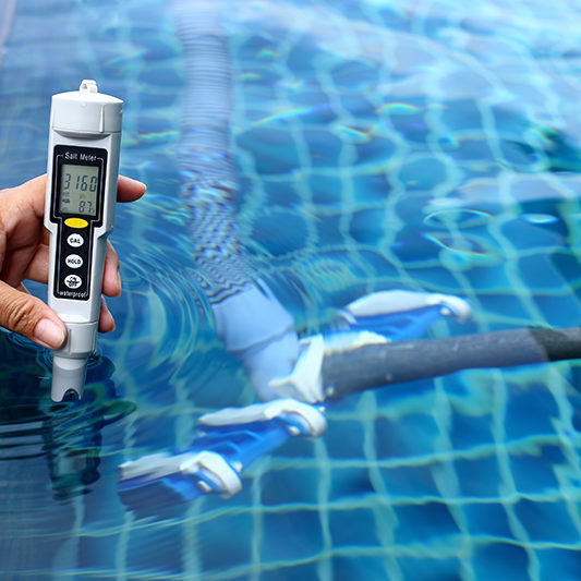 Hand holding salt meter tester in pool