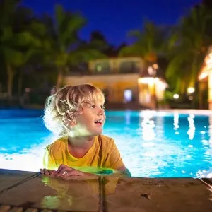 Kid popping up out of water at edge of pool at nighttime